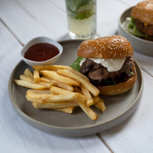 A lamb burger on a plate with a side of chips and sauce