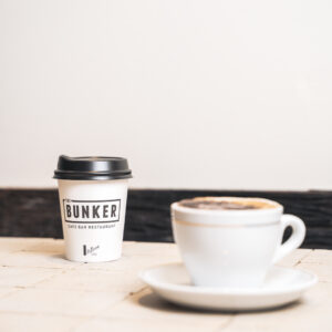 The Bunker-branded coffee takeaway cup next to a mug of freshly brewed coffee